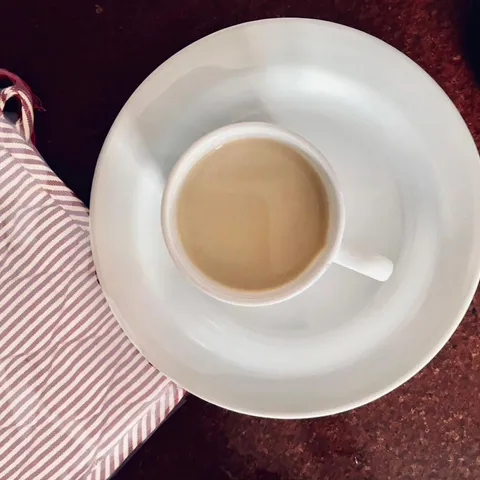 A white cup of creamy coffee milk tea on a white saucer beside a red-and-white striped napkin