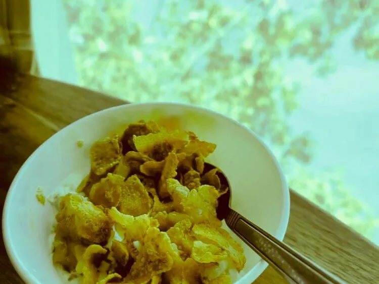 A white bowl of vanilla ice cream covered with syrup-coated cornflakes, with a spoon resting in it