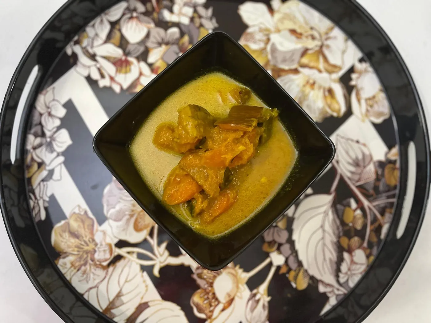 Sri Lankan pumpkin and carrot curry in a square black bowl on a floral serving tray