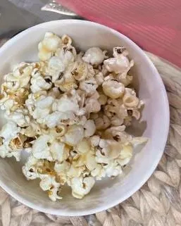 A white bowl of homemade stovetop popcorn on a woven placemat