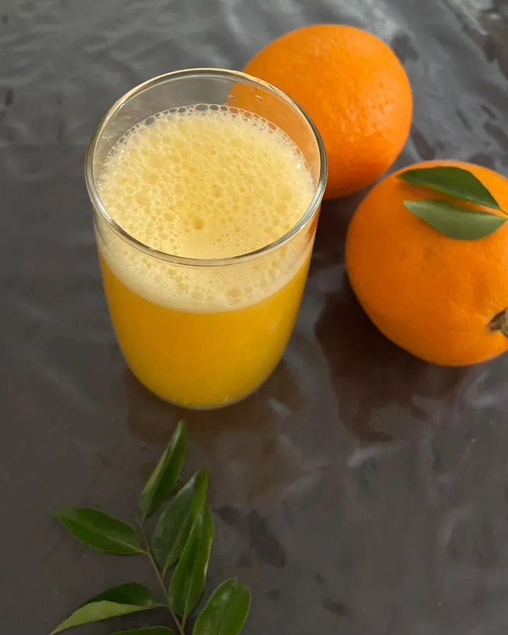 A glass of fresh homemade orange juice next to two whole oranges