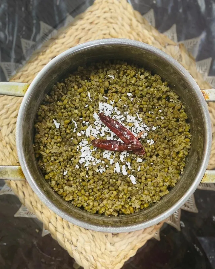 A pot of boiled green gram topped with scraped coconut and dried red chilies, on a woven mat