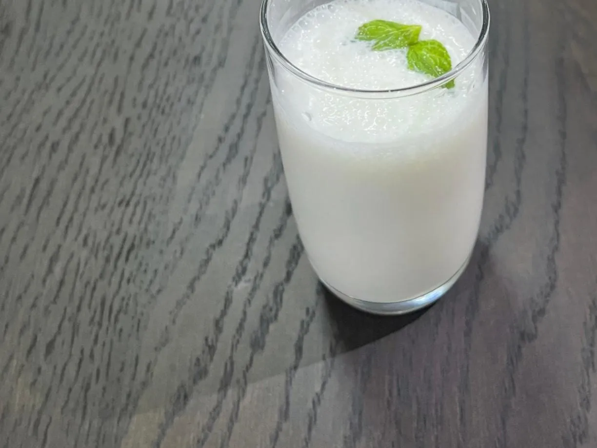 A tall glass of chilled laban yogurt drink garnished with mint leaves, on a dark wooden table