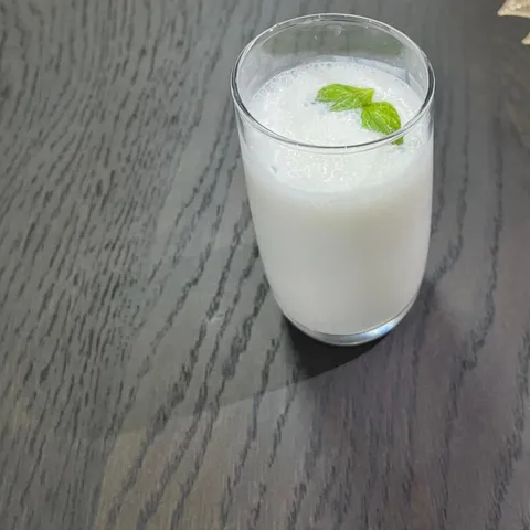 A tall glass of chilled laban yogurt drink garnished with mint leaves, on a dark wooden table