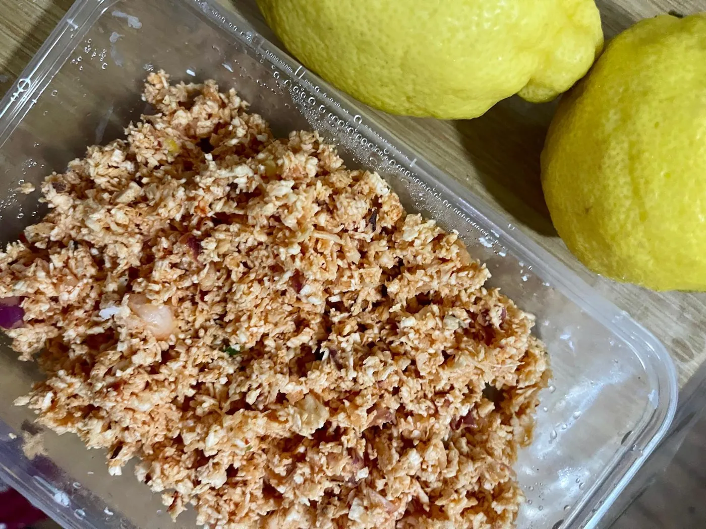 Coconut sambol in a clear container next to two whole lemons