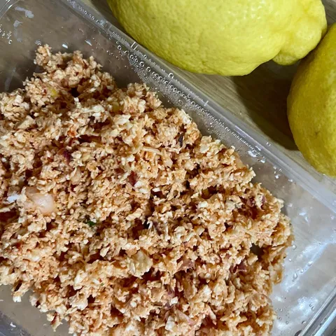 Coconut sambol in a clear container next to two whole lemons