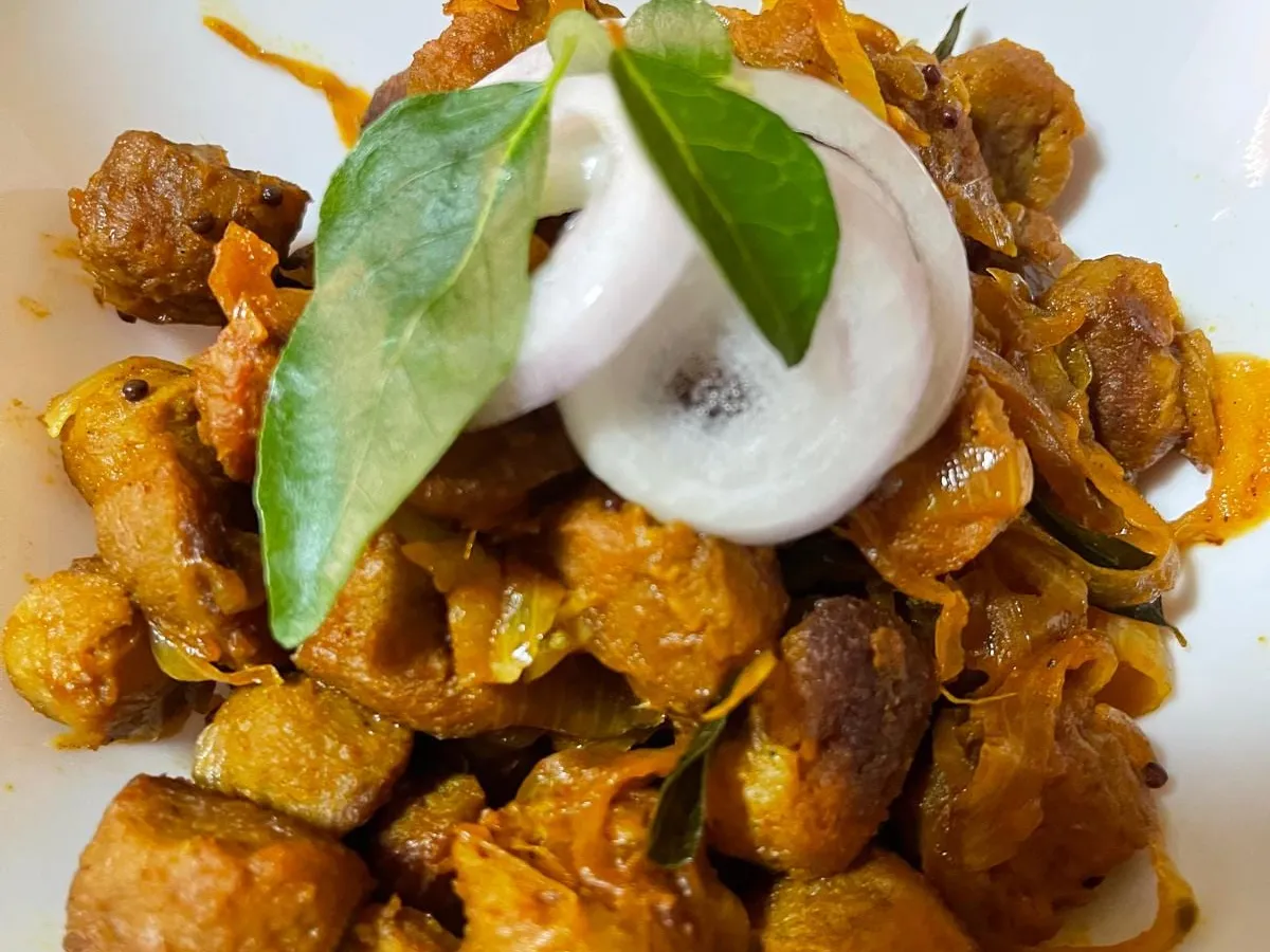 Soy meat chunks with sautéed onions on a white plate, garnished with onion rings and curry leaves