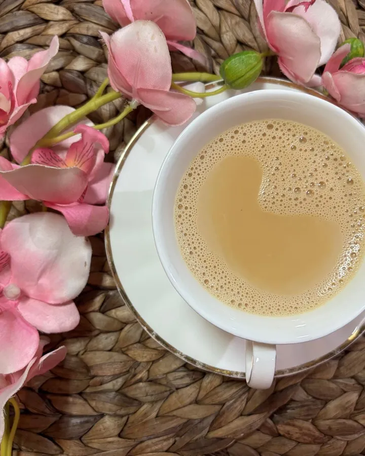 A cup of creamy milk tea on a white saucer, with pink orchids on a woven placemat