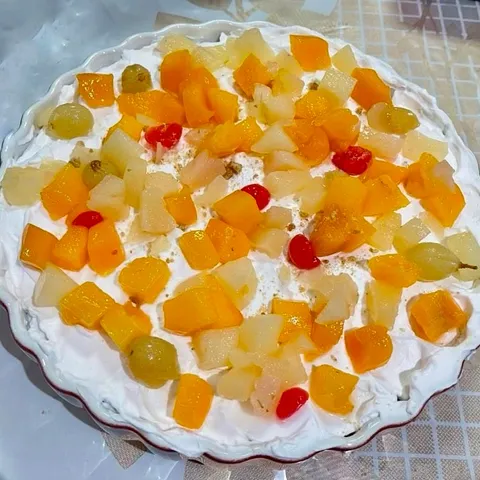 Fruit custard trifle in a white fluted dish, topped with whipped cream and colorful mixed fruit