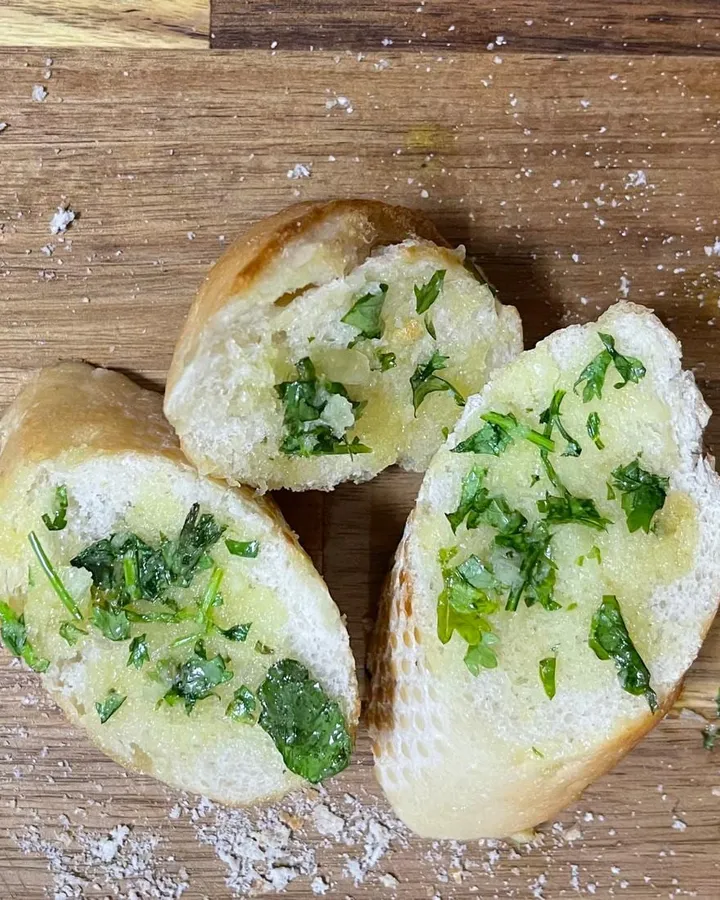 Three slices of garlic bread spread with green herb and garlic butter on a wooden board