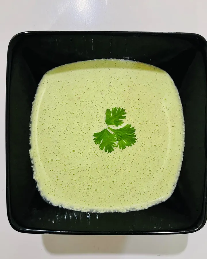 Smooth pale green chutney in a square black bowl, garnished with a single coriander leaf